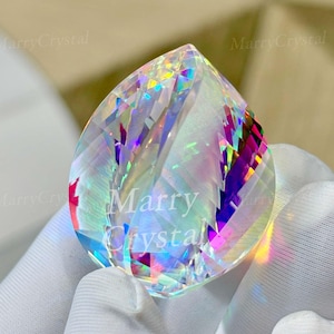 May include: A large, iridescent crystal in a teardrop shape. The crystal has a rainbow effect, with colors of pink, purple, and yellow. The text "Marry Crystal" is visible on the crystal. The crystal is held by a gloved hand.