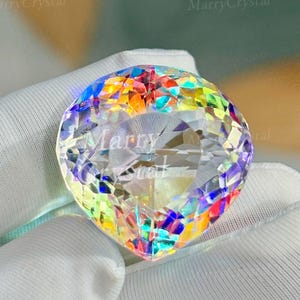 May include: A large, faceted crystal with a rainbow iridescence. The crystal is held in a white glove. The text "MarryCrystal" is visible on the crystal.