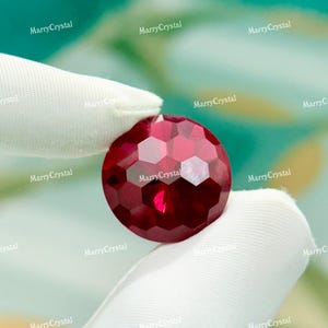 May include: A round, faceted, deep red gemstone with a honeycomb-like surface pattern. The stone displays a vibrant crimson hue and reflects light through its multiple geometric facets, creating a clear, polished appearance throughout the piece.