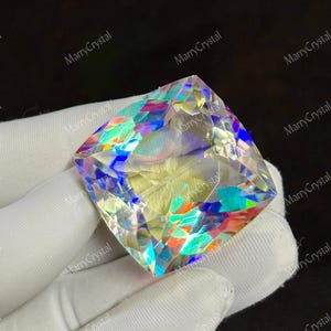 May include: A large, square-cut gemstone with a rainbow iridescence. The gem displays a spectrum of colors, including blues, greens, and yellows, reflecting light. The image is set against a dark background, highlighting the gem's brilliance.