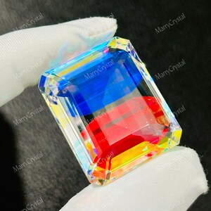 May include: A large, rectangular crystal with vibrant colors of blue, red, and yellow. The crystal is held by a gloved hand. The text "MarryCrystal" is printed on the crystal.