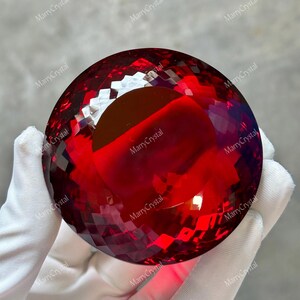May include: A deep red, spherical crystal object featuring a multifaceted, geometric surface pattern that reflects light. The item is translucent, displaying a rich crimson hue throughout its rounded form, with the text MarryCrystal visible.