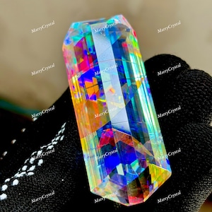 May include: A large, faceted crystal with a prismatic effect, displaying a spectrum of colors including blue, green, yellow, and red. The crystal is held against a black background. The text "MarryCrystal" is repeated on the background.