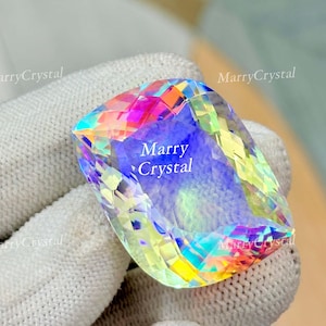 May include: A large, rectangular gemstone with a rainbow iridescence. The gem has a faceted cut, displaying a spectrum of colors including pink, yellow, blue, and green. The text "MarryCrystal" is visible on the gem.