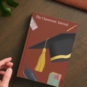 May include: A brown hardcover journal titled The Classroom Journal featuring a graphic illustration of a black graduation cap with a yellow tassel, a ruler, a pencil, and a stack of colorful notebooks on the front cover.