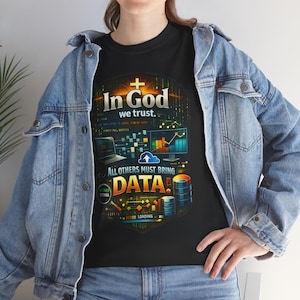 Può includere: T-shirt nero con un design grafico con la scritta "In God we trust." e "All others must bring data." Il design include una croce, schermi di computer e simboli di archiviazione dati. La maglietta è indossata con una giacca di jeans.