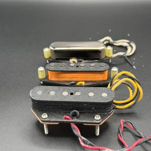 May include: Two electric guitar pickups. The front pickup has a black fiber bobbin with six silver pole pieces and yellow and black lead wires. The rear pickup features a copper-wound coil, six silver pole pieces, and a chrome cover with white wires.