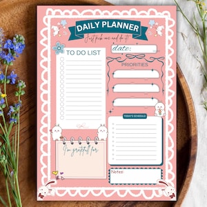 Könnte beinhalten: Ein rosafarbener Tagesplaner-Bogen mit weißem Wellenrand, Zeichentrick-Hasen und türkisfarbenen Überschriften. Der Text umfasst "DAILY PLANNER," "Just pick one and do it!," "TO DO LIST," "date:," "PRIORITIES," "TODAY'S SCHEDULE," "I'm grateful for:," und "Notes."
