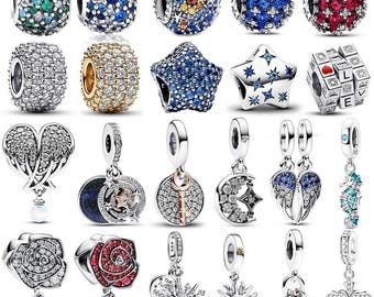 Puede incluir: Una colección de veinte dijes de metal con diversos diseños, incluyendo esferas incrustadas con cristales azules, verdes, rojos y transparentes, formas de estrellas, un cubo con la palabra LOVE, alas en forma de corazón, llaves, lunas, rosas y cruces.