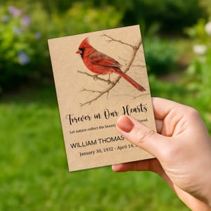 May include: A beige card with a watercolor illustration of a red cardinal perched on a branch. The text "Forever in Our Hearts" is above the text "Let nature reflect the beauty". Below is the name "WILLIAM THOMAS" and dates.