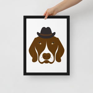 May include: Framed art print featuring a brown dog wearing a black fedora hat. The dog has brown eyes, a white patch on its face, and a brown nose. The artwork is set against a white background and framed in a black border.