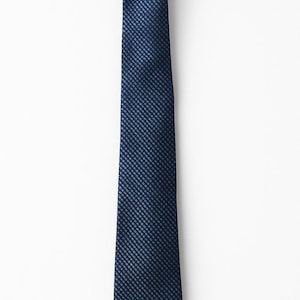 Puede incluir: Una corbata azul marino con un patrón texturizado de cuadrados repetidos. La corbata es de color liso y se muestra sobre un fondo blanco. Un accesorio clásico para ocasiones formales.