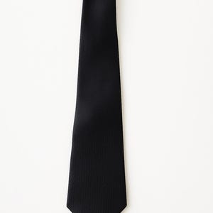 May include: A solid black necktie with a textured surface. The tie is displayed against a white background. The tie is a classic accessory for formal or business attire.