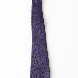 May include: A purple paisley tie with a repeating pattern in silver and black. The tie is a classic accessory, suitable for formal or business attire. The fabric has a subtle sheen, enhancing the intricate design.