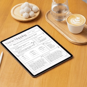 May include: A digital tablet displaying a "Verse Mapping" worksheet, alongside a white stylus. A wooden tray holds a glass of water and a cup of coffee with latte art. A small wooden plate with white, round treats is also present.