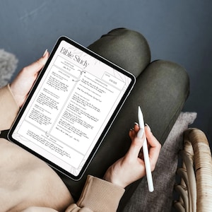 May include: A digital tablet displaying a "Bible Study" worksheet with text and diagrams. A white stylus rests in the hand of a person holding the tablet. The person is wearing a beige sweater and dark green pants.