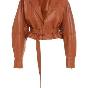 May include: A brown leather jacket with a belted waist and long sleeves. The jacket has a notched collar and a long belt that hangs down. The jacket is a medium brown color.