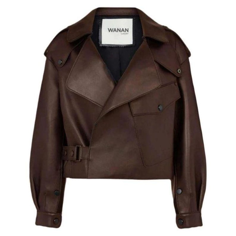 May include: A brown leather jacket with a unique asymmetrical design. The jacket features a notched collar, two front pockets, and a belt at the waist. The label "WANAN" is visible on the inner collar.