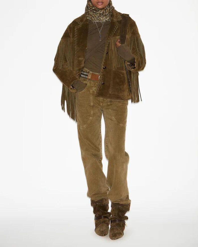 May include: A full-length shot of a person wearing a brown suede jacket with fringe, a brown turtleneck, corduroy pants, and brown suede boots. The jacket has a button closure and a belt. The outfit is a monochromatic ensemble.
