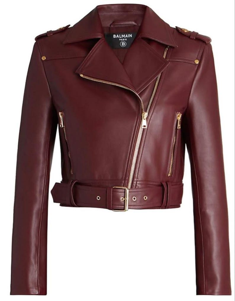May include: A burgundy leather motorcycle jacket with a notched collar, asymmetrical zipper, and gold-tone hardware. The jacket features a belted waist, shoulder epaulets, and multiple zippered pockets. The brand name "BALMAIN PARIS" is visible on a tag.