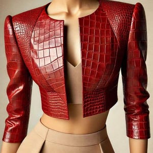 May include: A cropped, red jacket with a textured, crocodile-like pattern. The jacket features a round neckline, long sleeves, and a tailored fit. The open front reveals a neutral-toned top and a pleated skirt.