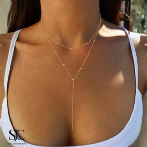 Può includere: Una collana dorata a più strati dal design delicato. La collana presenta due fili, uno più corto e uno più lungo, con piccole perline distanziate uniformemente. Il filo più lungo si estende a forma di Y, creando un look elegante.