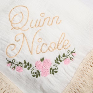 May include: White cotton baby blanket with a gold embroidered name "Quinn Nicole" and pink embroidered flowers.