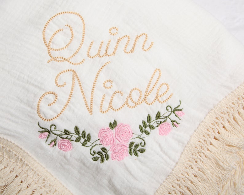May include: White cotton baby blanket with a gold embroidered name "Quinn Nicole" and pink embroidered flowers.