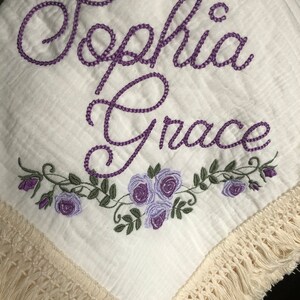 May include: White muslin baby blanket with purple embroidered lettering "Sophia Grace" and a floral design with purple roses.