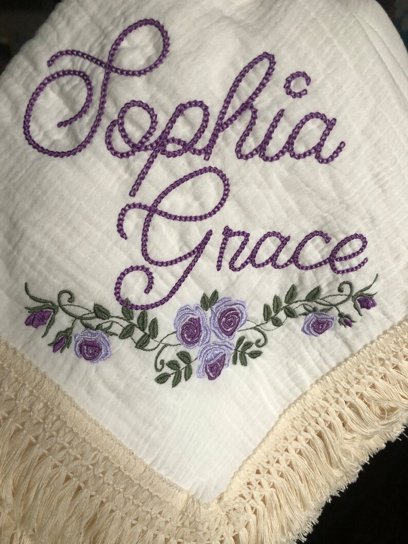 May include: White muslin baby blanket with purple embroidered lettering "Sophia Grace" and a floral design with purple roses.