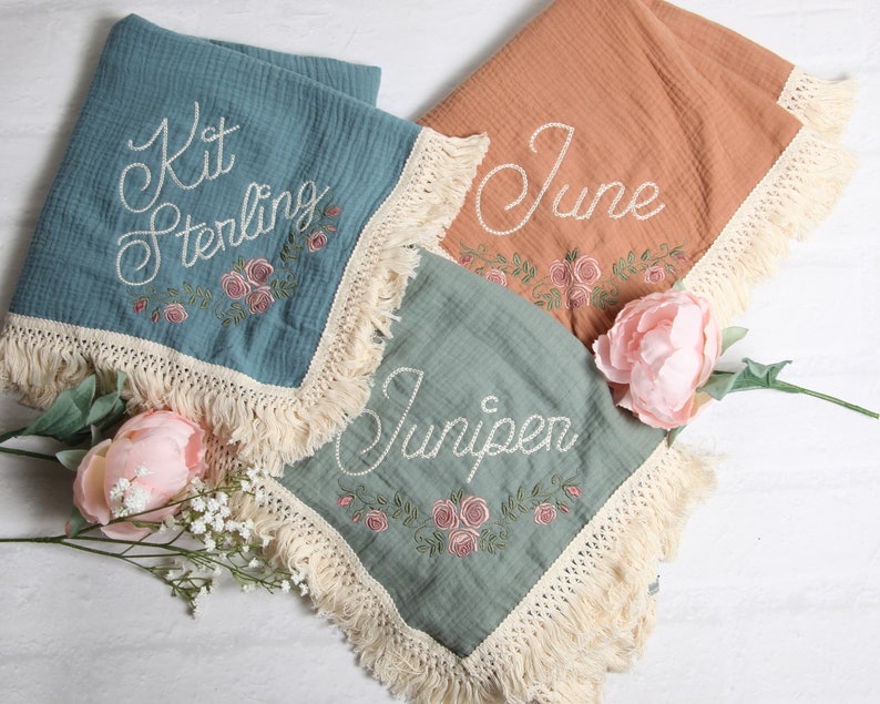 May include: Three personalized baby blankets with embroidered names and floral designs. The blankets are made of soft, lightweight fabric and have a fringe trim.