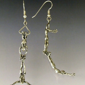 May include: A pair of silver earrings featuring a dangling design of three stylized figures, each holding onto the one above. The figures are connected by a thin silver chain.