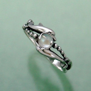 May include: A silver ring with two dolphins intertwined around a round, iridescent moonstone.