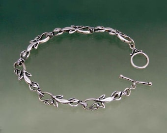 May include: A silver bracelet with a delicate chain design featuring stylized leaves. The bracelet has a toggle clasp.