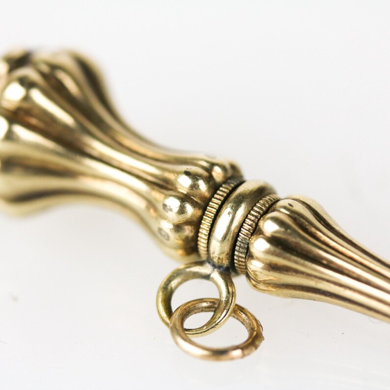 May include: A gold-toned, ornate, decorative, pencil-shaped, pocket-sized, object with a loop for attaching to a chain.
