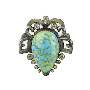 May include: Vintage brooch with a silver-tone metal filigree design. The brooch features a large, teardrop-shaped, light blue and yellow speckled stone at the center, surrounded by clear rhinestones.