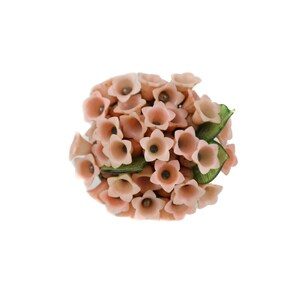 May include: A cluster of pink glass flowers with green leaves. The flowers are arranged in a bouquet shape.
