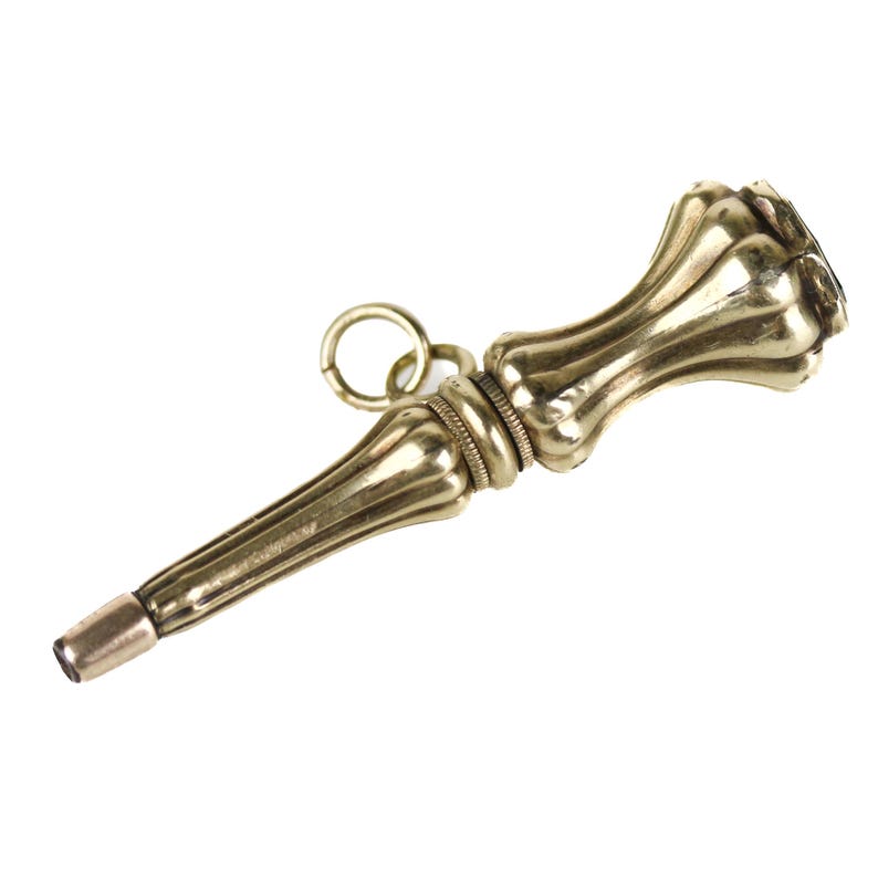 May include: A gold-toned pocket watch key with a decorative, fluted handle and a ring at the top.