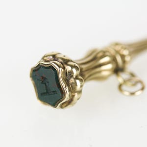 May include: A gold seal with a green gemstone and a decorative design. The seal is attached to a gold chain.