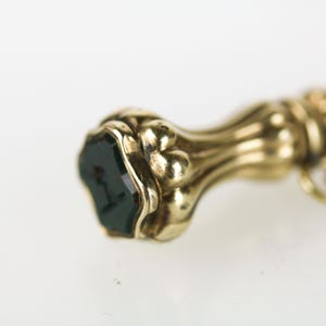 May include: A gold seal with a dark green gemstone set in the top. The seal has a decorative, ornate design.