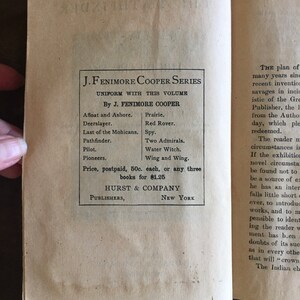 May include: A vintage book cover for the J. Fenimore Cooper Series. The cover is printed in black ink on a cream-colored paper background. The title of the series is "J. Fenimore Cooper Series" and the subtitle is "Uniform with this volume". The author's name is listed as "By J. Fenimore Cooper". The cover lists several titles by the author, including "Afloat and Ashore", "Prairie", "Deerslayer", "Red Rover", "Last of the Mohicans", "Spy", "Two Admirals", "Water Witch", "Wing and Wing", "Pilot", and "Pioneers". The cover also includes the price of the books, which is 50 cents each or $1.25 for any three books. The publisher is listed as "Hurst & Company, Publishers, New York".
