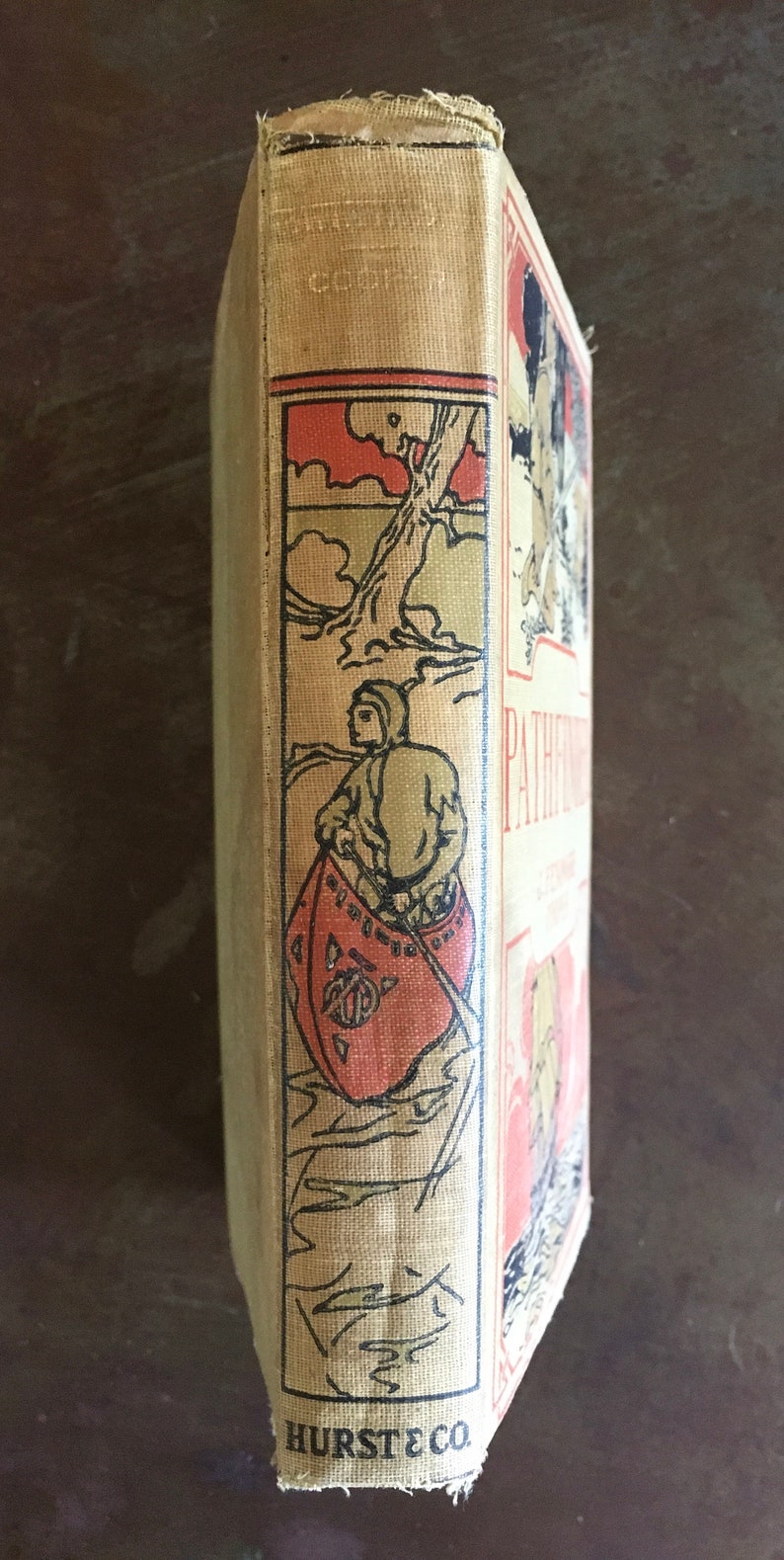 May include: A vintage book with a tan cloth cover and black and red illustrations. The title "Pathfinder" is visible on the spine. The book is published by Hurst & Co.