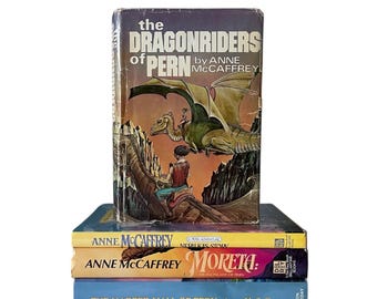May include: A stack of four paperback books featuring the Dragonriders of Pern series by Anne McCaffrey. The top book has a colorful cover with a dragon and rider. The other books have yellow, blue, and light blue covers with the title and author's name.