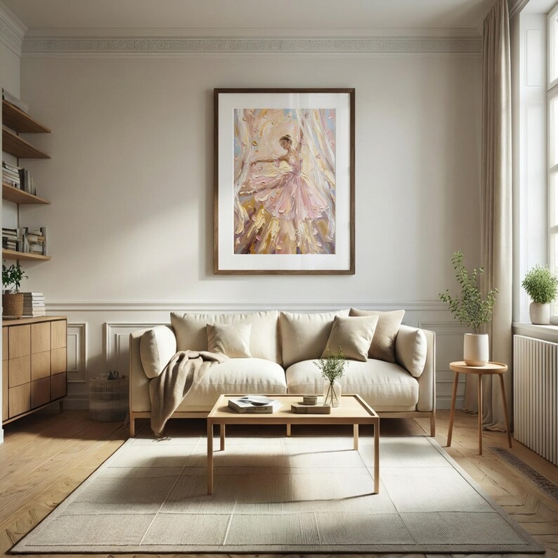 以下が含まれることがあります： ピンクのドレスを着たバレリーナを描いた額装アートプリント。ベージュのソファの上に飾られています。ピンク、ゴールド、白の色調で描かれた柔らかな筆致が、明るく開放的な空間で踊るダンサーの動きを捉えています。