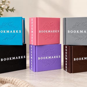 May include: Six rectangular boxes in blue, pink, grey, black, purple, and brown, each featuring the word BOOKMARKS embossed on the front and side. The front of each box displays a debossed leaf design surrounding the text in white lettering.