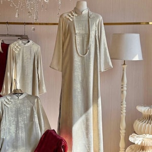 A four-panel, shimmering silk (lụa nhũ) Áo dài featuring a straight, flowing silhouette and frog closures, paired with sparkling red pants