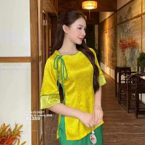 Puede incluir: Una mujer con un top de satén amarillo con ribetes verdes y pantalones verdes. El top tiene cuello redondo y mangas cortas. El conjunto es de la colección Rubi Closet Basic & Luxury 2024, con el número #3389. El texto "DuyenDangAoDai" está en la parte inferior.