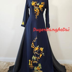 Könnte beinhalten: Marineblaues Langarmkleid mit gelber Blumenstickerei. Das Kleid hat einen hohen Ausschnitt und einen fließenden Rock mit schwarzem Overlay. Der Text "DuyenDangAoDai" ist auf dem Kleid sichtbar.