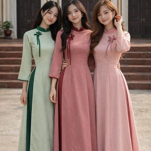 Puede incluir: Tres mujeres con vestidos largos y elegantes. Los vestidos son en tonos verde claro, rosa empolvado y rosa pálido, cada uno con un panel lateral en contraste. Los vestidos tienen cuellos mandarín y adornos decorativos.