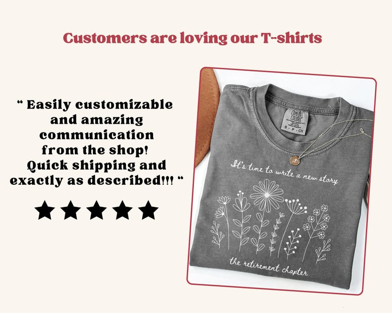 May include: A charcoal gray t-shirt featuring a white line art graphic of various wildflowers. The text on the shirt reads, "It's time to write a new story" above the flowers and "the retirement chapter" below them. The shirt has a crew neckline.